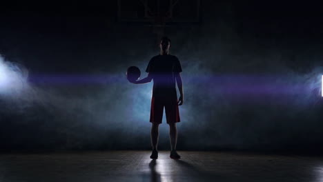 Male-athlete-in-sportswear-and-sneakers-throws-a-basketball-and-catches-him-in-the-hands-in-smoke-and-slow-motion